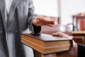 partial view of woman giving oath on holy bible in courtroom during deposition process