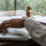 close up on a person's hands using a laptop and referencing a notebook on the table working for a court reporting company