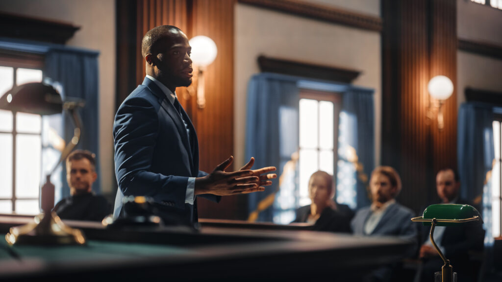 lawyer standing up in a court room speaking to the jury while a shadow jury listens