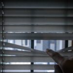 Peeking through window blinds. Hand separating the slats of the window curtain with fingers to look out at process server to avoid being served