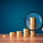 stack of coins going from small stack to larger stack with hand holding magnifying glass on largest stack to demonstrate what is my case worth