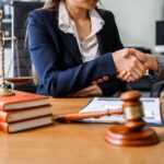 two female lawyers in blue business suits shaking hands at wooden desk after deciding whether it is better to go to trial or settle their case