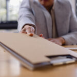 businessman handing over a brown folder across the desk containing an errata sheet